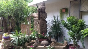 A garden with a stone statue, various potted plants, and a stone wall. - Casa Berastegui (Puerto Colombia)