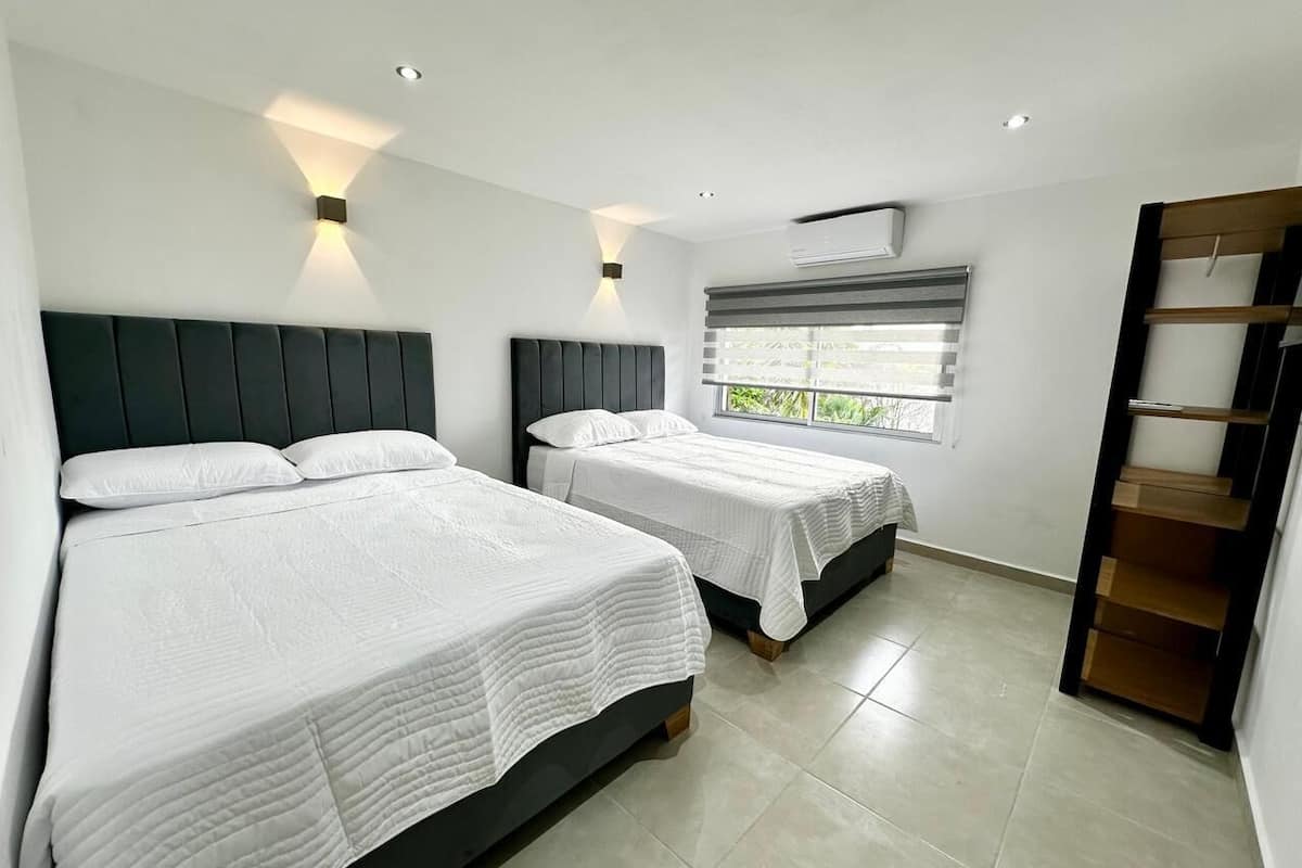A modern hotel room with two beds, a built-in shelf, and a window with blinds.