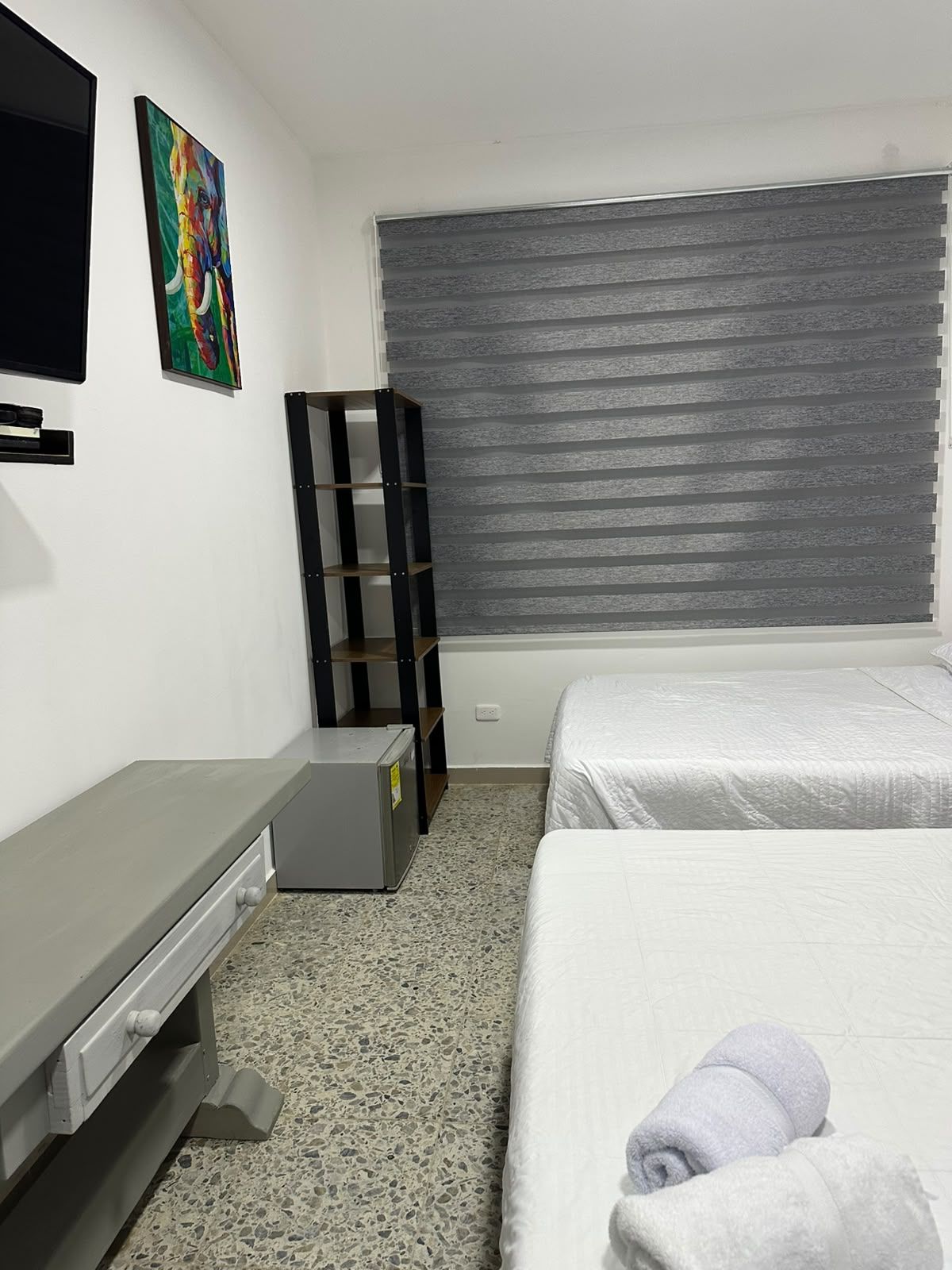 Une chambre à coucher avec un lit, un bureau, une chaise, un téléviseur et une fenêtre avec des stores.