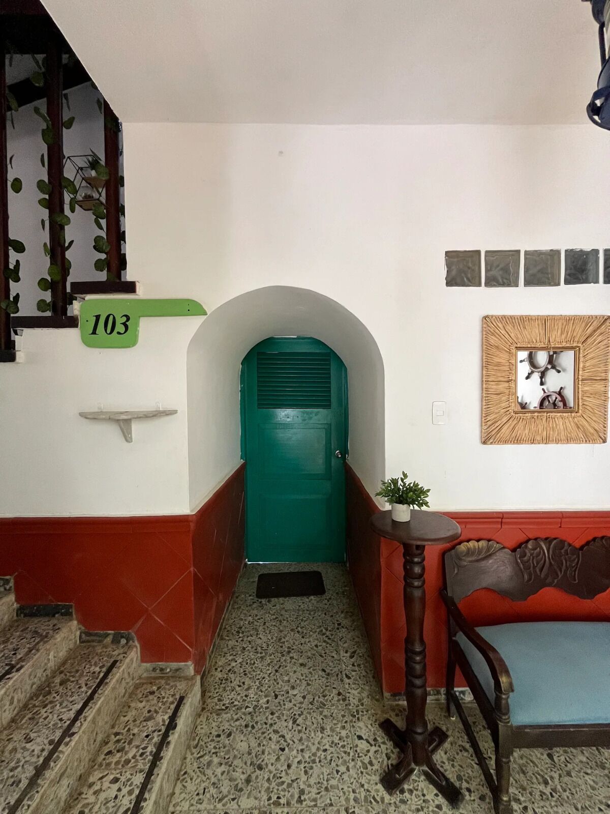 A hallway with a green door, a staircase, a chair, and a wall-mounted mirror.