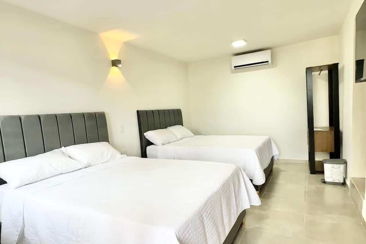 A hotel room with two beds, a wall-mounted air conditioner, and a small trash bin.