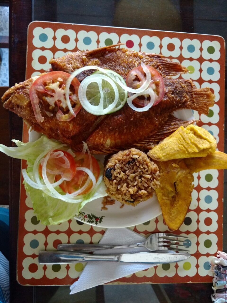 Un plato con un pescado frito entero, arroz, tajadas de plátano frito y una ensalada.