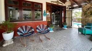 A covered outdoor area with two rocking chairs, a pool, and a stone wall. - Casa Berastegui (Puerto Colombia)