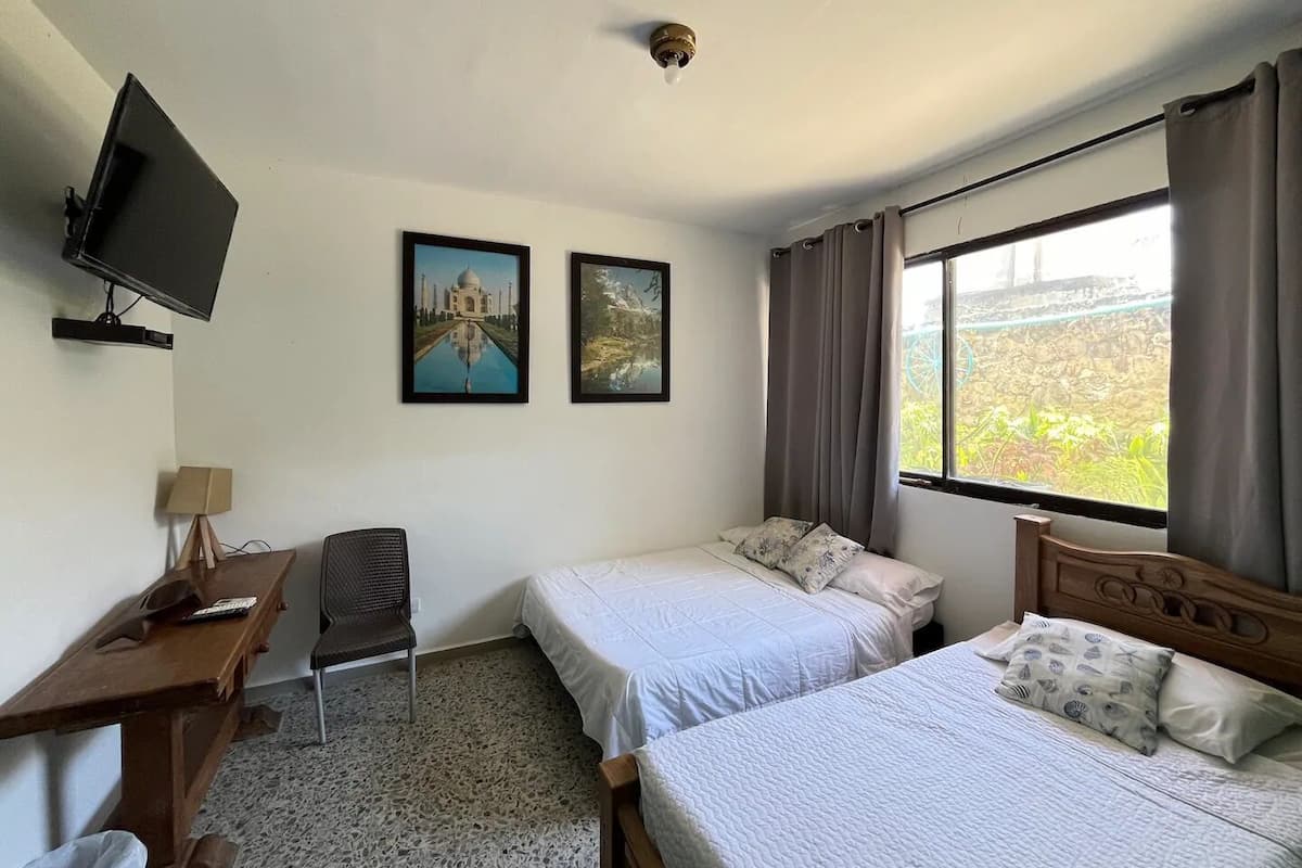 A hotel room with two beds, a desk, a chair, a television, and two framed pictures on the wall.