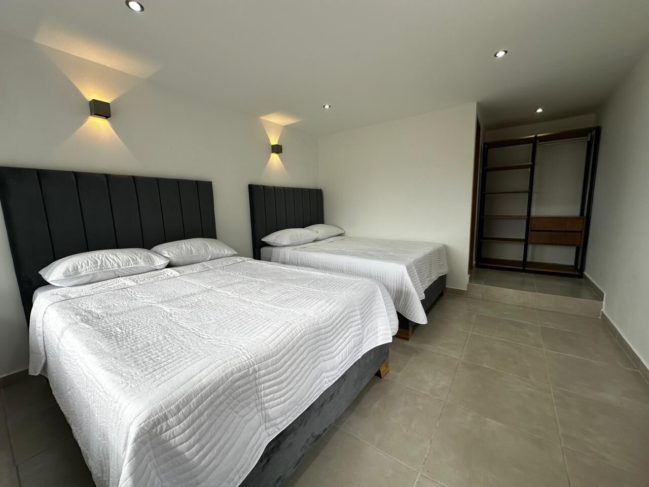 Una habitación de hotel moderna con dos camas, un cabecero oscuro e iluminación empotrada en el techo.