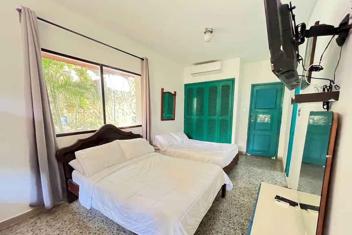A hotel room with a bed, a TV, a window with curtains, and a door.