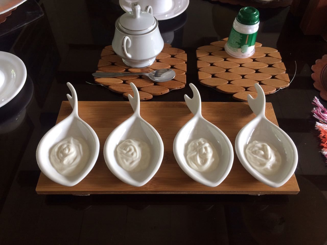 Four white ceramic spoons with a swirl design on a wooden tray.