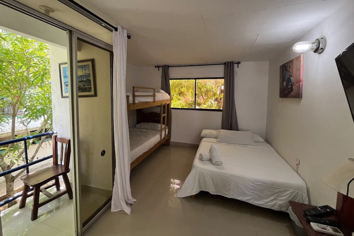 A room with bunk beds, a desk, a chair, a window with curtains, and a TV on the wall.