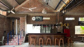 A rustic bar area with a brick wall, wooden stools, and a bar counter. - Casa Berastegui (Puerto Colombia)