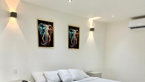A modern bedroom with a large bed, white bedding, two wall-mounted light fixtures, and two framed artworks. - Casa Berastegui (Puerto Colombia)