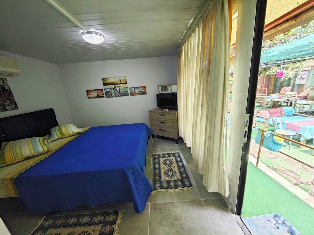 Ein Schlafzimmer mit Bett, Fernseher, Kommode und Blick auf einen Außenbereich mit Tischen und Stühlen.