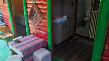 Quarto compacto com uma pequena mesa e banco, uma porta para o banheiro e um tapete de boas-vindas.