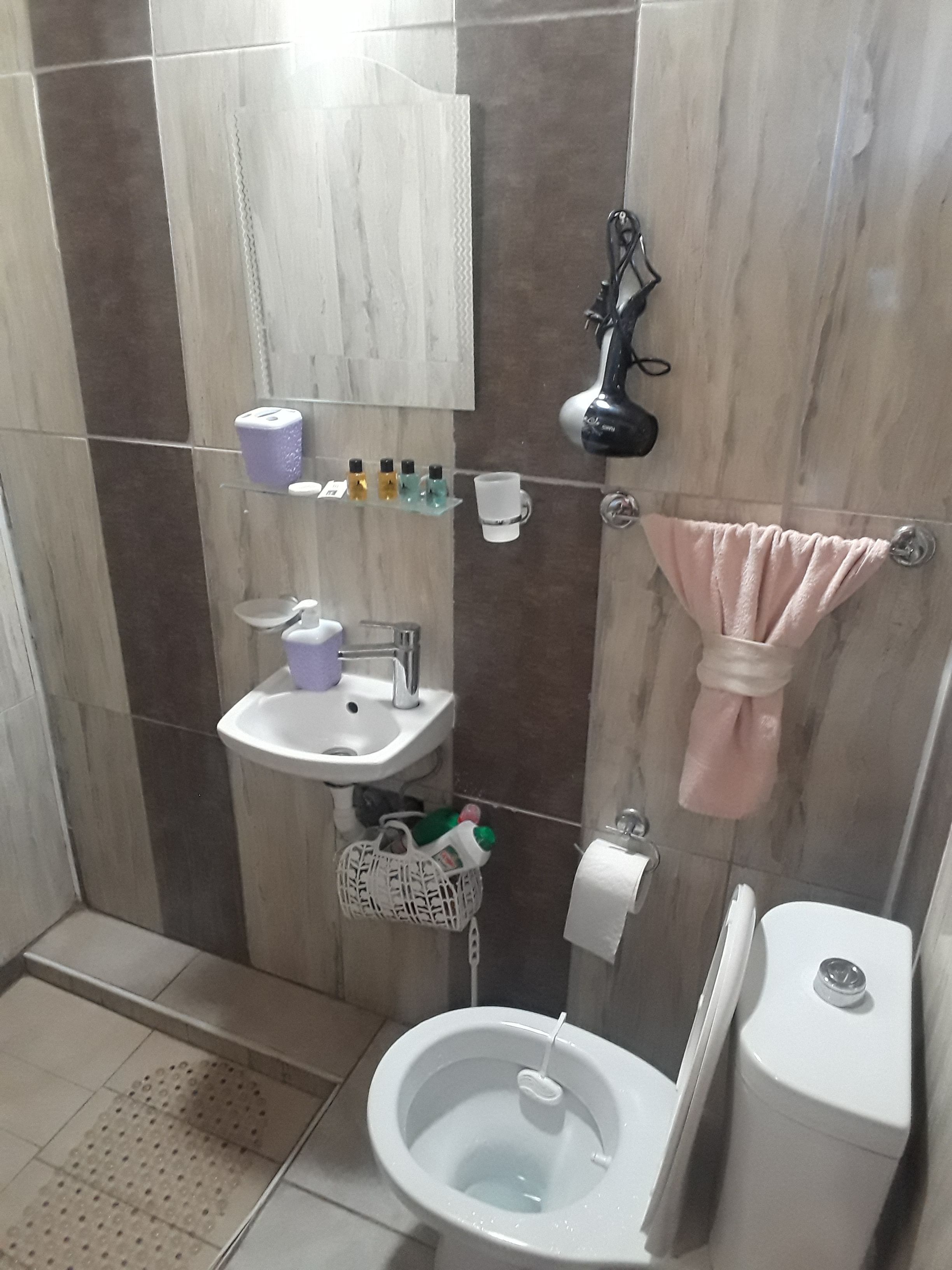 A bathroom with a toilet, sink, and mirror. There are toiletries on the sink and a towel hanging on the wall.