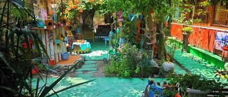 A vibrant garden with a variety of potted plants and flowers, a small table, and a rustic wooden structure.