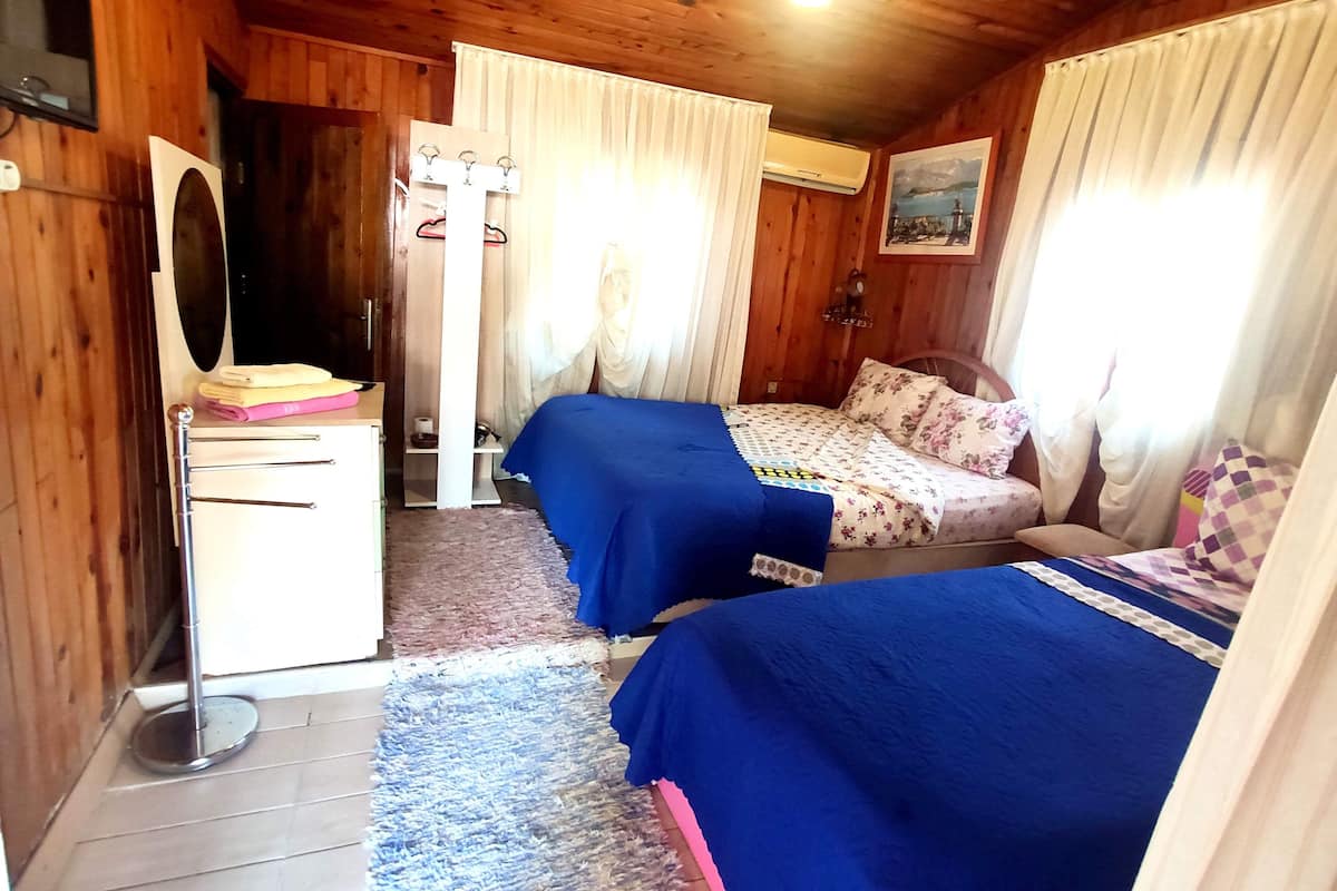 A room with two beds, a wooden wardrobe, a mirror, and a window with curtains.