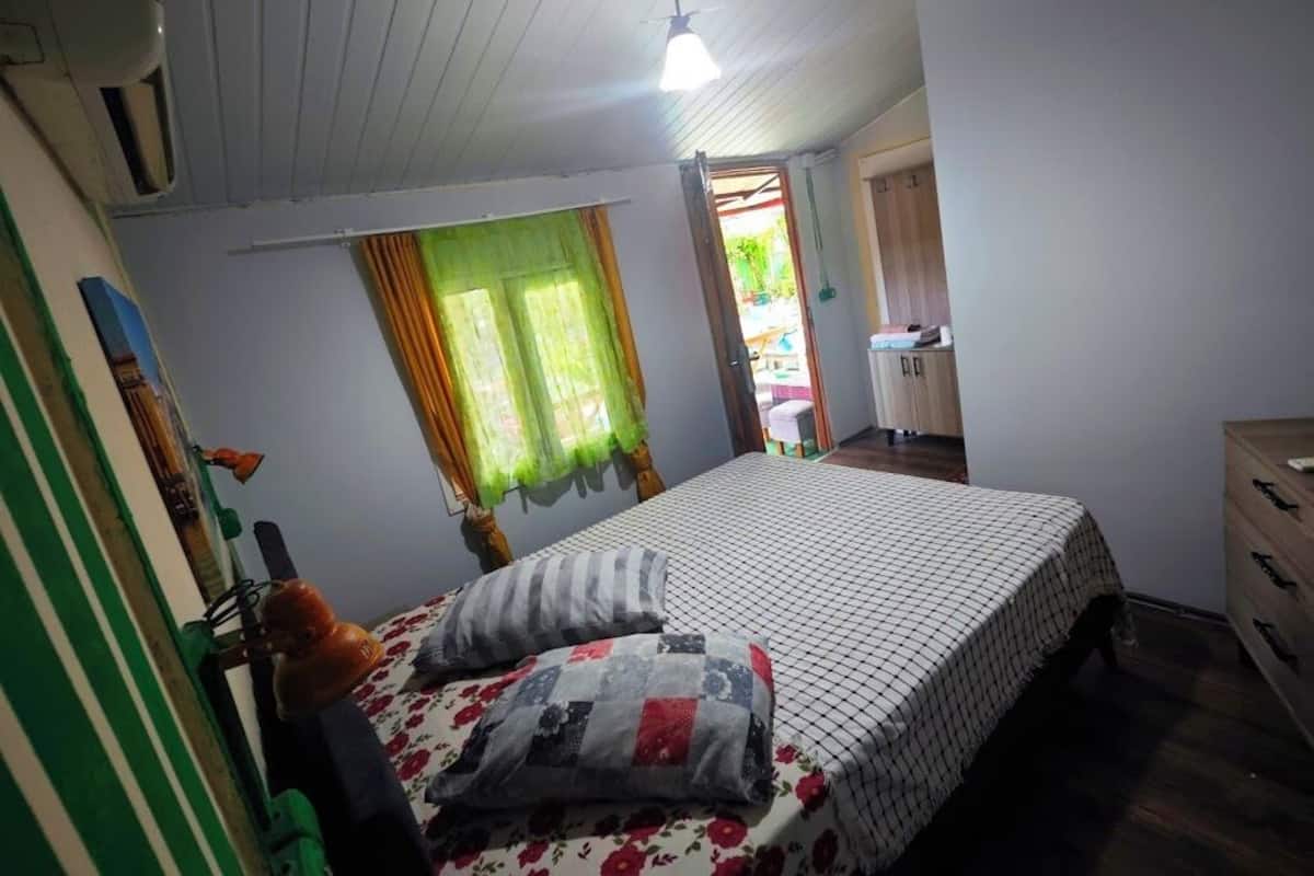 A bedroom with a bed, a dresser, a window with curtains, and a ceiling fan.