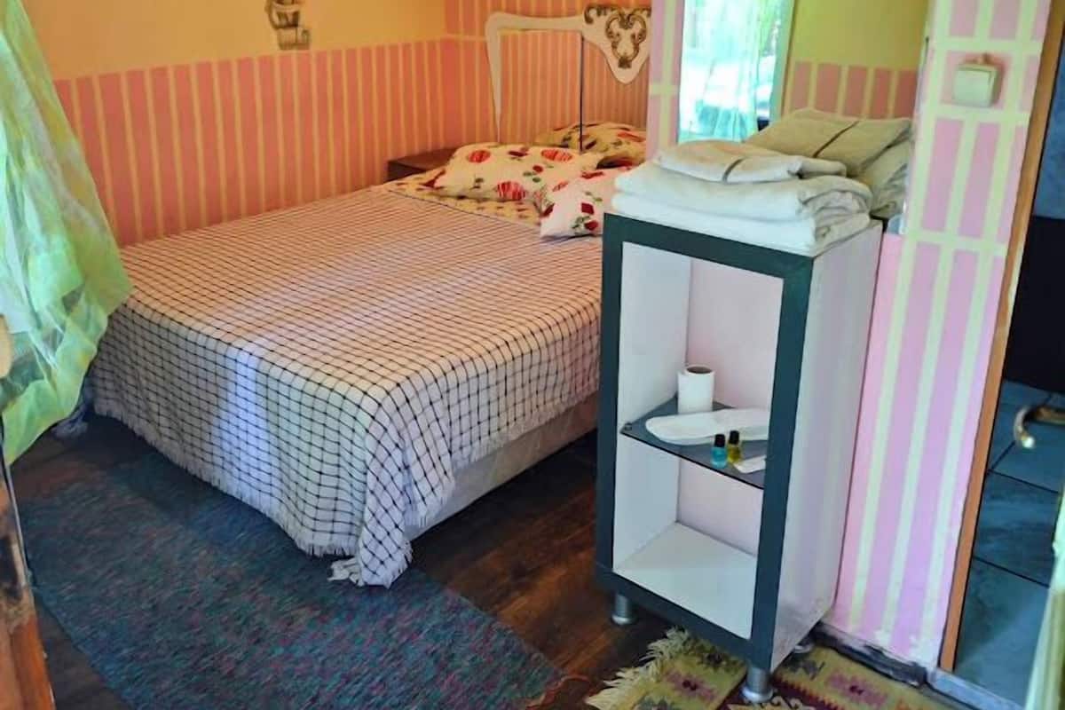 A bedroom with a bed, a bedside table, a mirror, and a window.