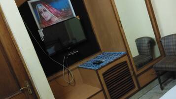 A room with a wooden wardrobe, a television, a mirror, and a bed.