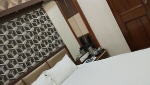 Een hotelkamer met een bed, een houten garderobe, een nachtkastje met een lamp en een wand met een geometrisch patroon.