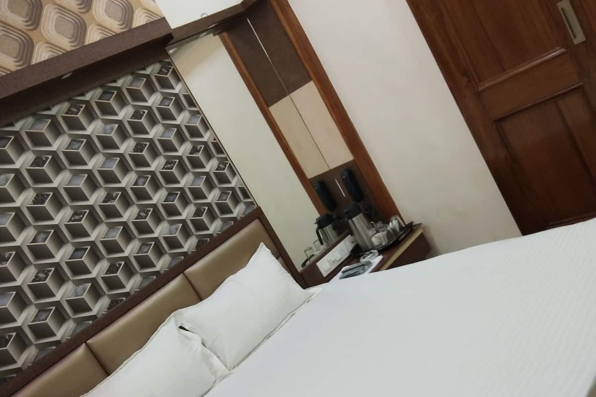 A hotel room with a bed, a wooden wardrobe, a nightstand with a lamp, and a geometric patterned wall.