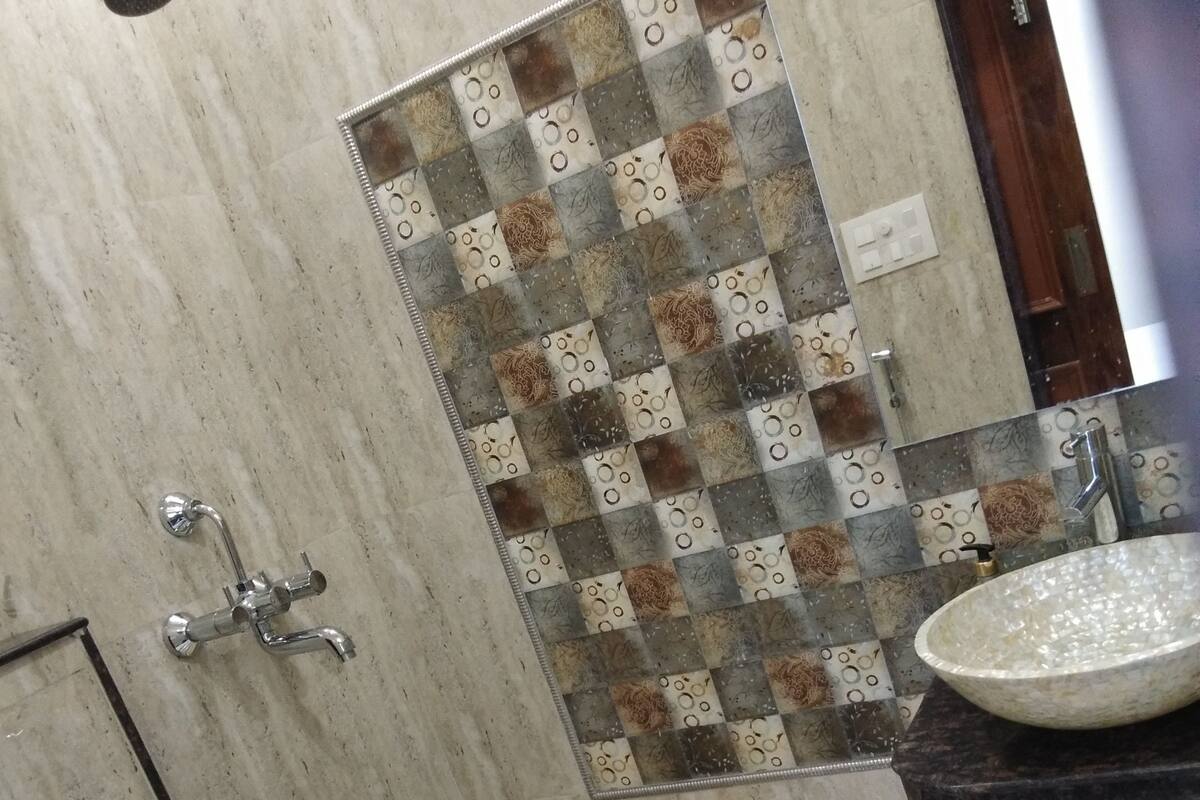 A bathroom with a tiled shower, a sink with a marble countertop, a toilet, and a small stool with a floral design.