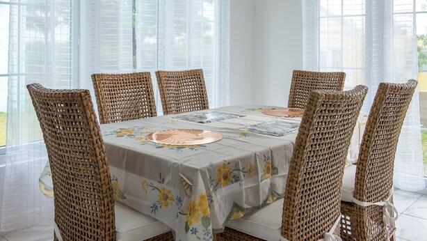 A dining area with a table covered in a floral tablecloth, surrounded by wicker chairs. - Paradise at Little Bay Cournty Club (Negril)