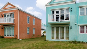 A row of two-story houses with balconies, a well-maintained lawn, and a clear sky. - Paradise at Little Bay Cournty Club (Negril)