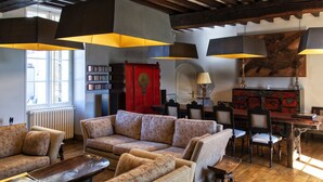 A cozy living room with a sofa, armchairs, a wooden coffee table, and a dining area with chairs and a table. There is a bookshelf, a red cabinet, and a painting on the wall. - Les Deux Abbesses en Vert (Mareuil en Périgord)