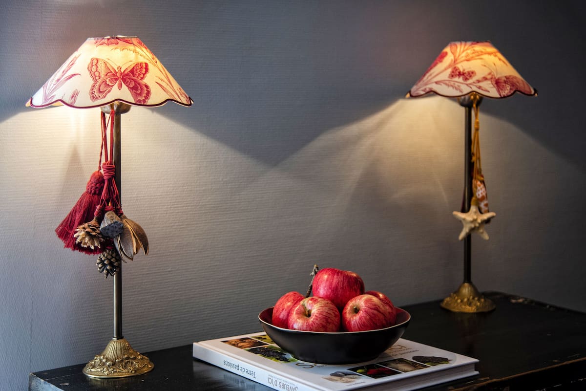 Deux lampes ornées de motifs de papillons sont posées sur une table, à côté d’un saladier rempli de pommes et d’un magazine.