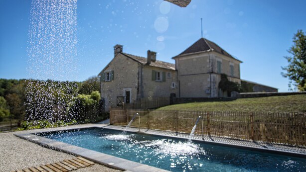 A swimming pool with a wooden structure above it, surrounded by a fence and a house in the background. - Les Deux Abbesses en Vert (Mareuil en Périgord)
