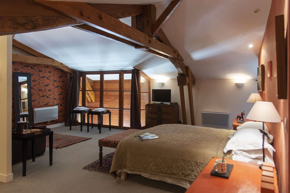 Une chambre à coucher avec un grand lit, un bureau avec une chaise, une télévision et une fenêtre avec des rideaux.