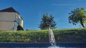A fountain with water spouting from a central point, surrounded by a grassy area with a building in the background. - Les Deux Abbesses en Vert (Mareuil en Périgord)