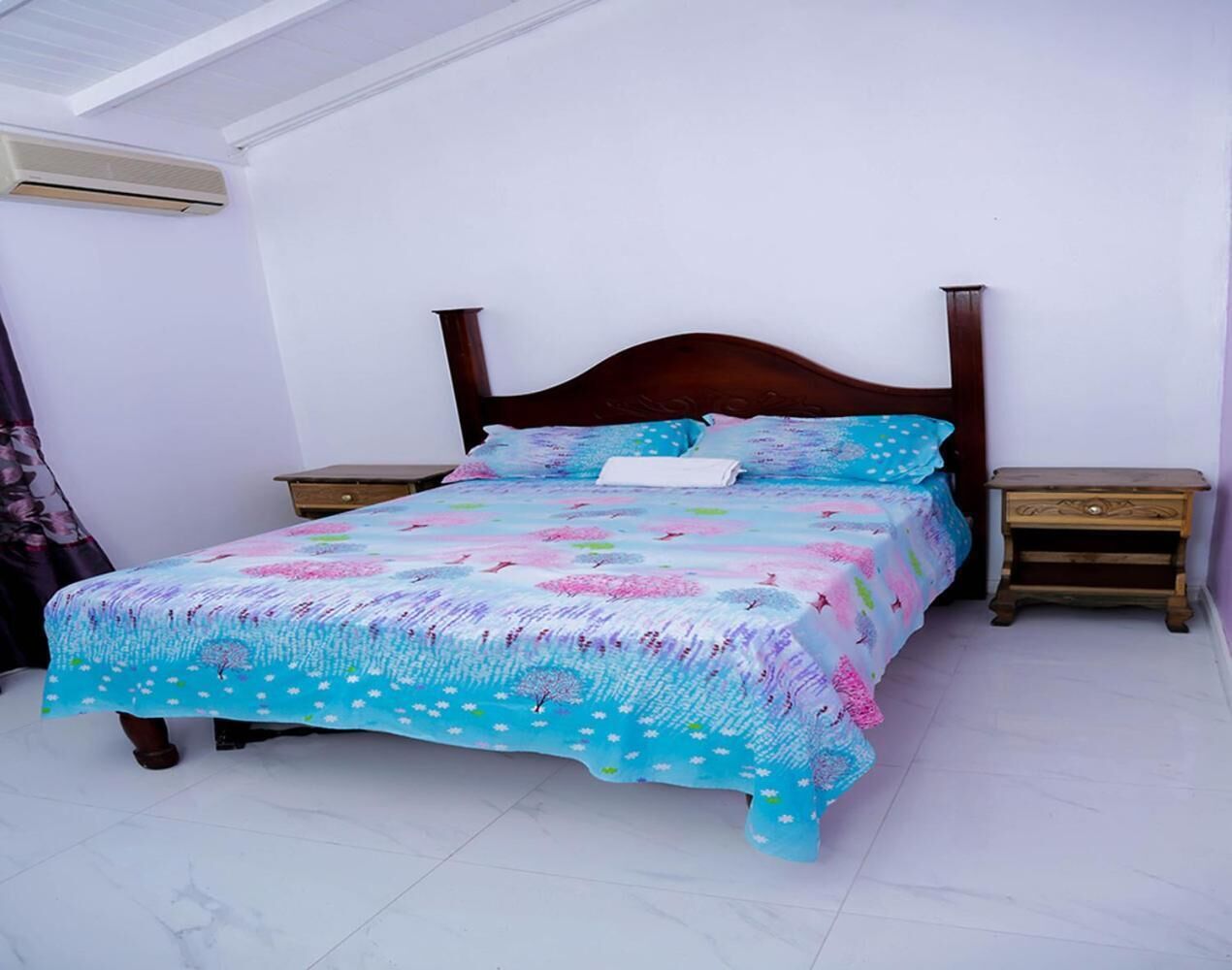 A bed with a floral bedspread, two nightstands, and an air conditioning unit on the wall.