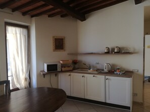 A kitchen with white cabinets, a wooden table, a microwave, and a kettle on the counter. - Camollia Suites (Siena)