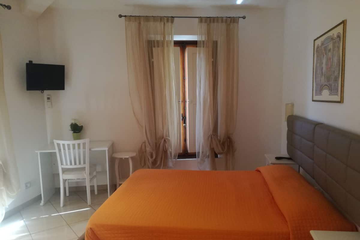 A hotel room with a bed, a desk, a chair, a television, and a door with curtains.