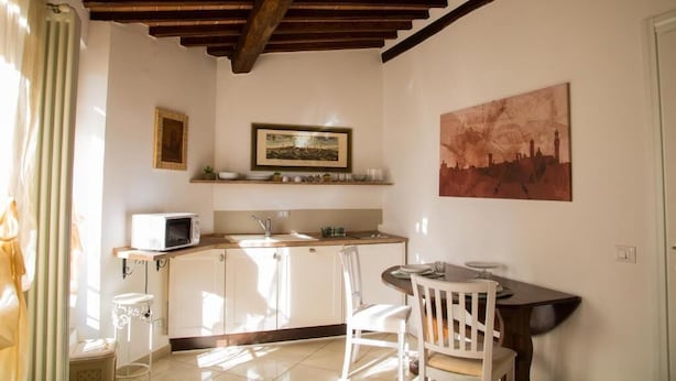 A compact kitchen with a microwave, sink, and a dining area with a table and chairs. - Camollia Suites (Siena)