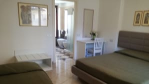 A hotel room with two beds, a desk, a chair, and a small seating area. - Camollia Suites (Siena)
