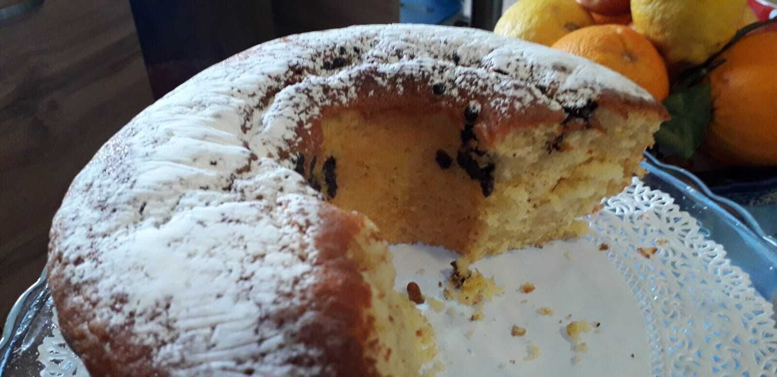 A round cake with a dusting of powdered sugar on top, partially sliced, on a blue plate with a white lace pattern.