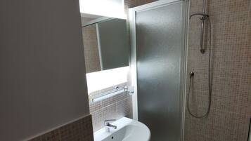 A bathroom with a glass shower enclosure, a sink, and a mirror.
