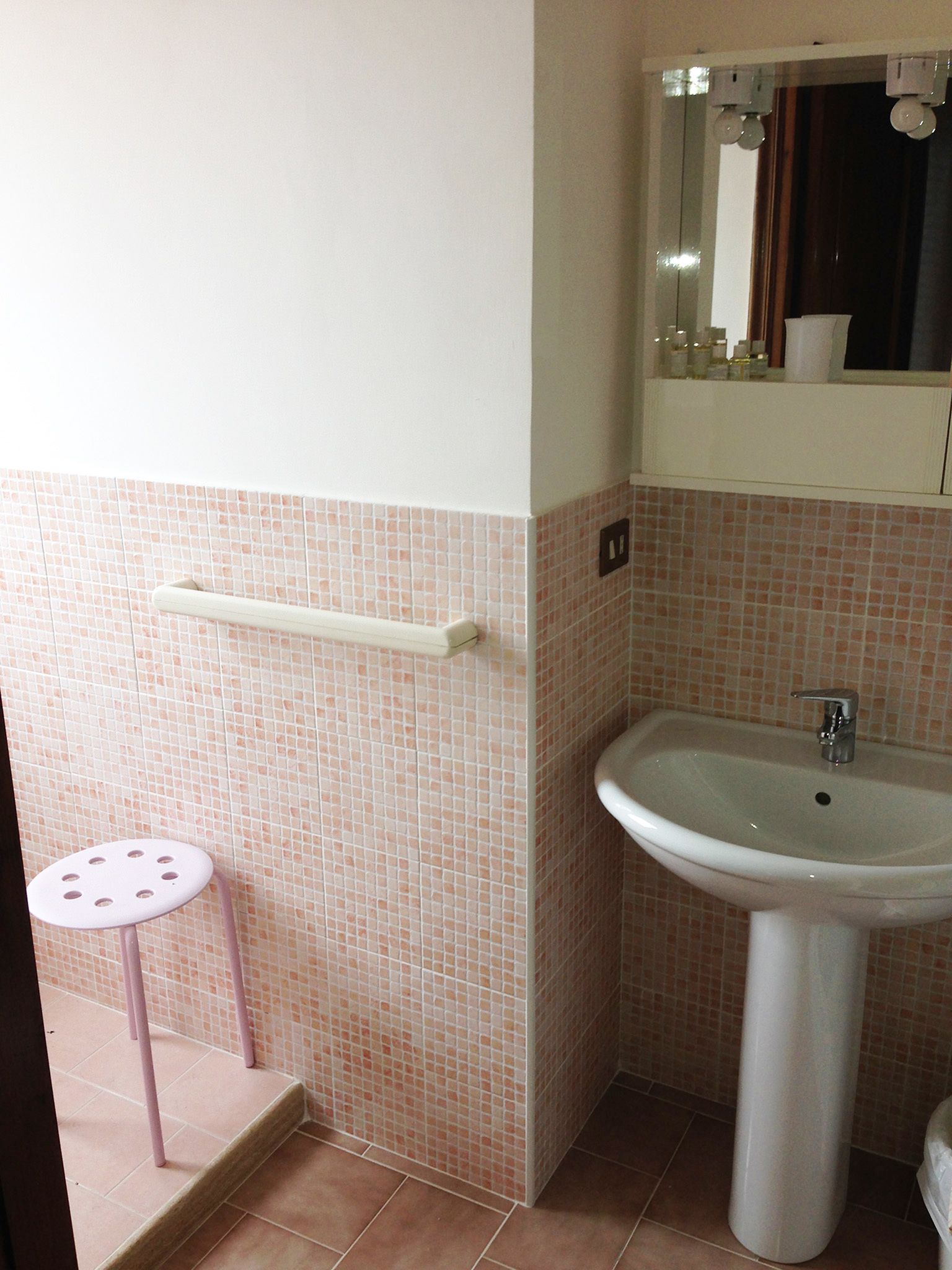 A bathroom with a sink, a mirror, and a small stool.