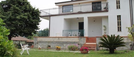 A two-story building with a balcony, a covered porch, and a small garden area with potted plants and a chair.