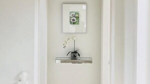 A hallway with a white wall, a framed picture, and a small vase with flowers. - The Chapel by Platinum Retreats (Andreas)