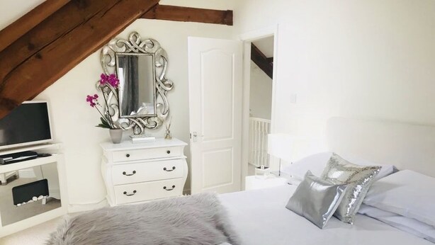 A bedroom with a bed, a dresser, a mirror, a television, and a door leading to another room. - The Chapel by Platinum Retreats (Andreas)