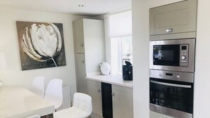 A modern kitchen with white cabinetry, a double oven, and a white dining table with chairs. - The Chapel by Platinum Retreats (Andreas)