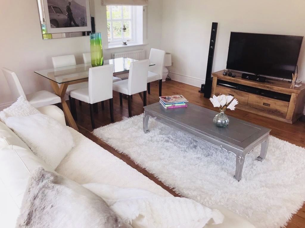 Un salon moderne avec un canapé blanc, une table basse en verre et un téléviseur posé sur un meuble en bois.