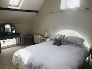 Een slaapkamer met dakraam, een bed met wit beddengoed, een dressoir en een spiegel.