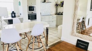 A modern kitchen with white cabinets, a tiled backsplash, and a wooden dining table with chairs. - The Chapel by Platinum Retreats (Andreas)