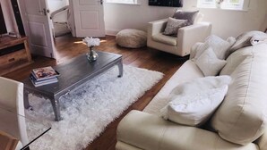 A living room with a white sofa, a coffee table, and a fluffy rug. - The Chapel by Platinum Retreats (Andreas)