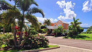A house with a white porch, surrounded by lush greenery and a clear blue sky. - Tropics at Little Bay Country Club (Negril)
