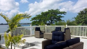 A deck with wicker furniture and a white railing overlooking a body of water. - Tropics at Little Bay Country Club (Negril)